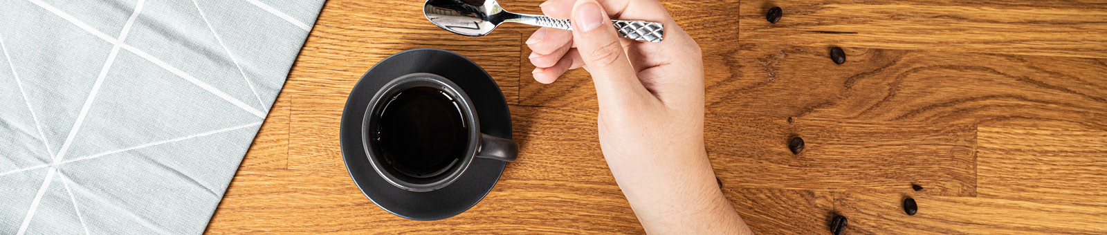 Das Bild zeigt eine Kaffeetasse und eine Hand die einen Löffel hält. 