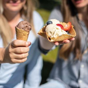 Das Bild zeigt zwei Frauen die ein Waffelhörnchen und eine Waffelschale mit Eis in die Kamera halten.