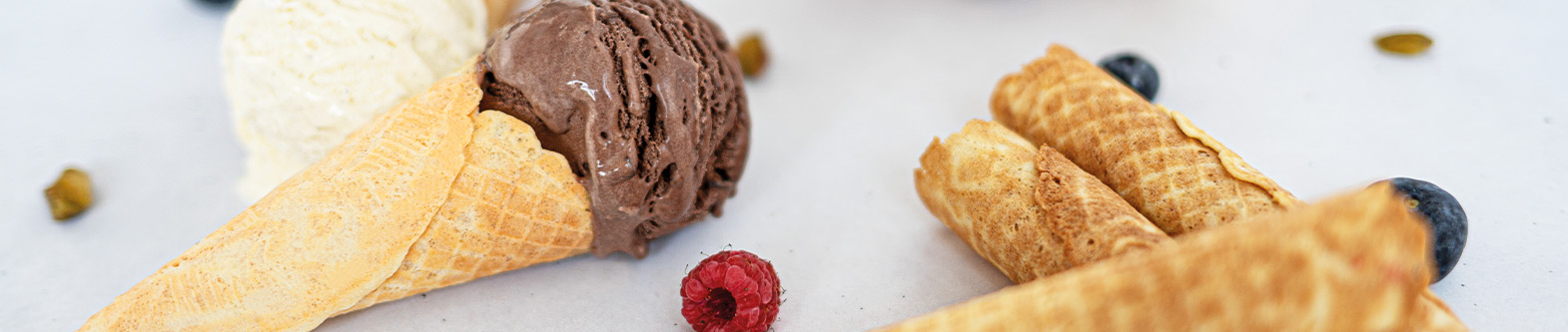 Das Bild zeigt Waffelhörnchen mit Schokoladen- und Vanilleeis und Beeren. 