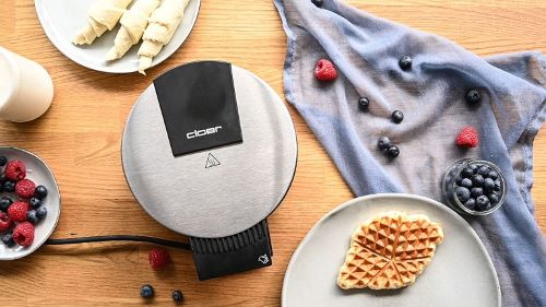 Blick von oben auf eine Holzarbeitsplatte auf der das Waffeleisen Cloer 189 und zwei Teller mit fertigen und rohen Croffles stehen. 