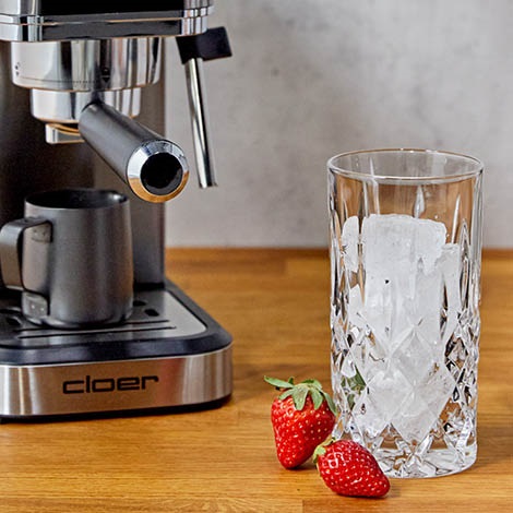 Das Bild zeigt ein Nachtmann Noblesse Longdrinkglas mit Eiswürfeln, im Hintergrund ist die Siebträgermaschine Cloer 5829 zu sehen.